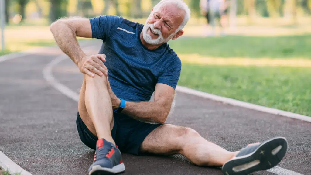 Man sitting on running track clutching knee in pain due to osteoarthritis