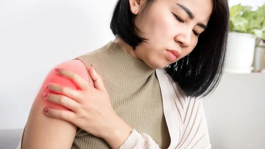 Woman holds her shoulder in pain, suffering from frozen shoulder before contacting an Austin physical therapist