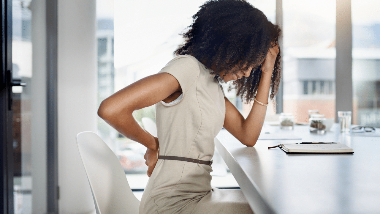 Woman holds back in pain at desk, needing Tips On Preventing Disc Herniation