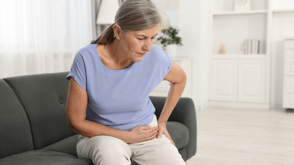 Woman holds hip in pain while sitting on couch and wondering: What Is Gluteus Medius Tendinopathy?