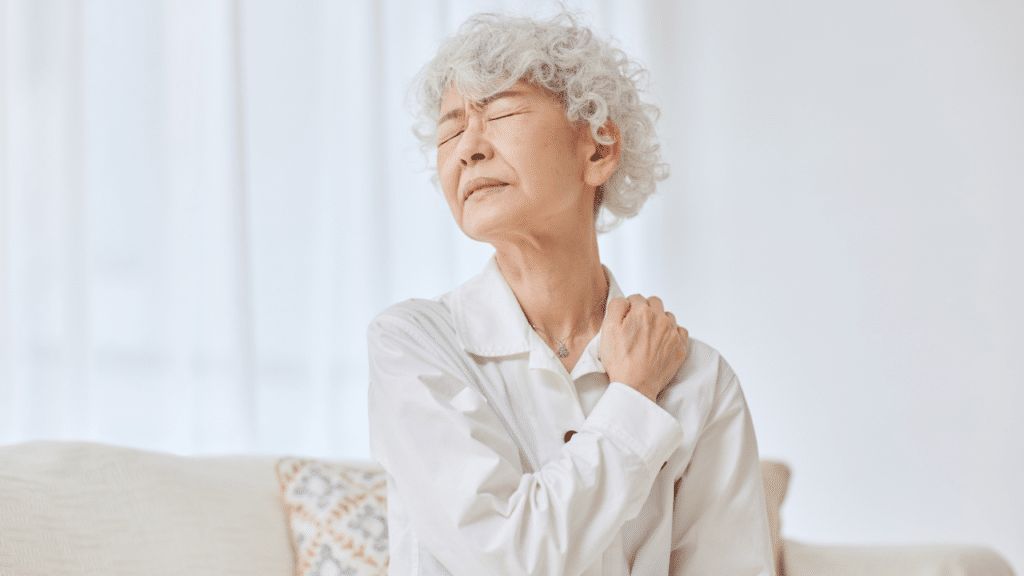 Older woman holds shoulder in pain wondering Why Shoulder Pain Spikes in Women in Their 40s to 60s
