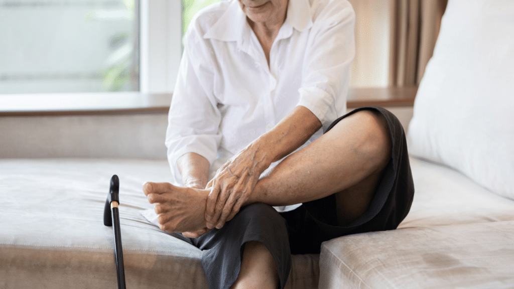 Person sits on bed holding foot in pain next to their cane, thinking of Neuropathy FAQs for an Austin, Texas physical therapist
